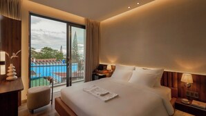 A hotel room with a large bed, a desk, a chair, a nightstand, a lamp, and a view of a swimming pool.