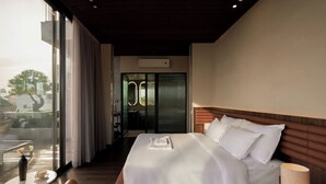 A modern hotel room with a large bed, a bedside table, a lamp, and a view of the outdoors through a large window.