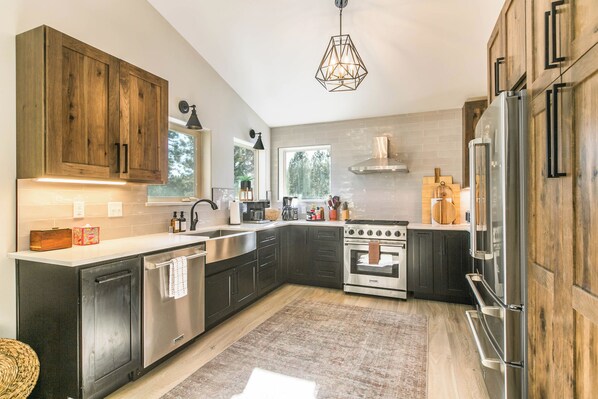 A modern kitchen with dark cabinetry, stainless steel appliances, and a large window providing natural light. - Modern Home w/Hot Tub, All Bedrms w/En Suite, Deck w/Gas Fire, Near Golf/Biking (Angel Fire)