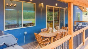 A covered outdoor dining area with a wooden table and chairs, a grill, and a view of the surrounding landscape.