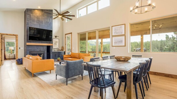 A spacious living area with a fireplace, large windows, and a dining table with chairs.