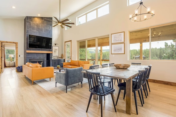 A spacious living area with a fireplace, large windows, and a dining table with chairs.
