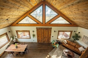 Ein geräumiges Loft mit hoher Decke, Holzbalken und großen Fenstern mit Blick ins Freie.
