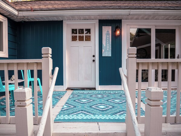 A front porch with a white door, a welcome sign, and a patterned rug. - Charming 2-bedroom cottage with WiFi, AC in Spring Lake (Spring Lake)