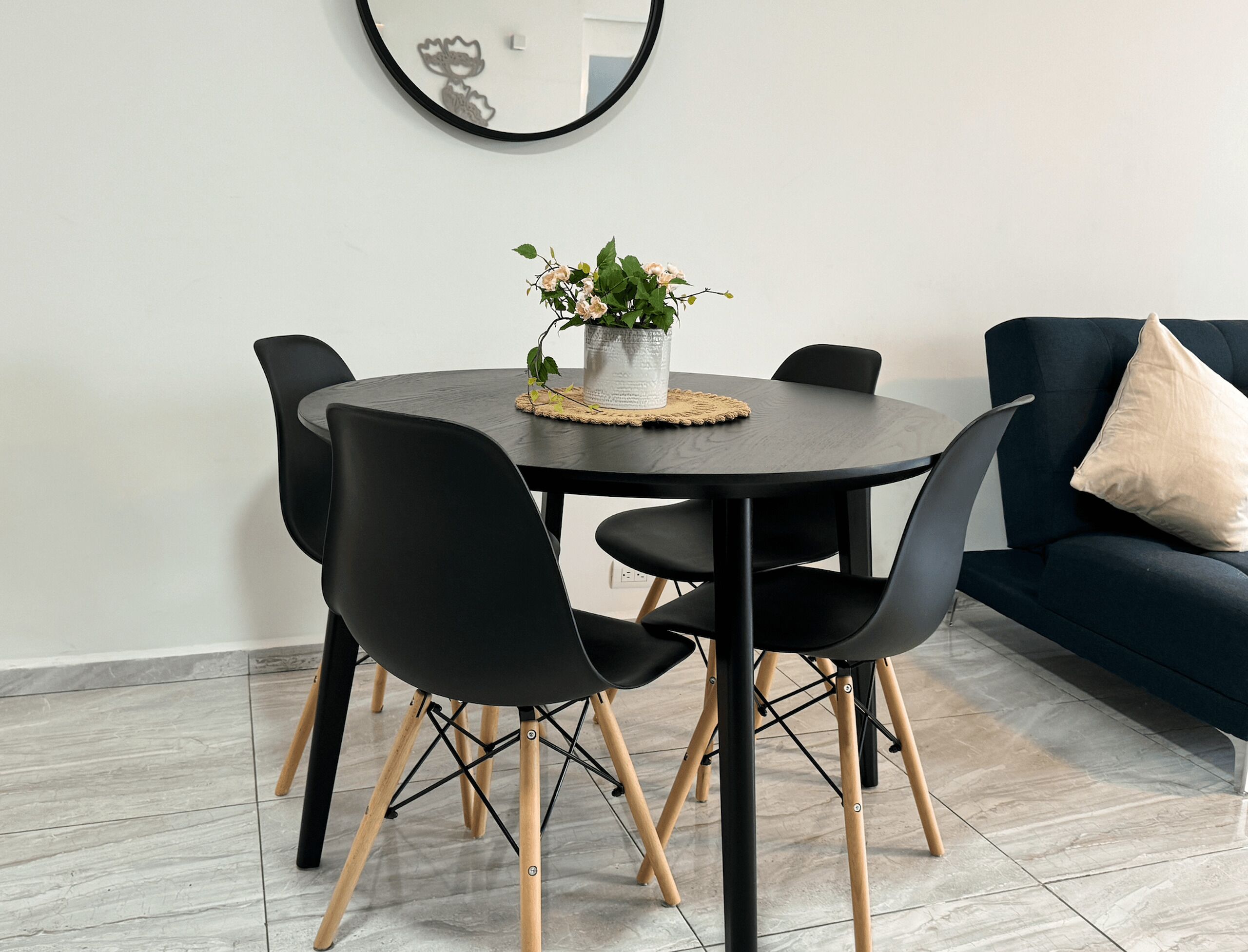 A modern dining area with a round table, black chairs, and a vase with flowers.