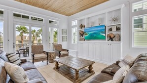 Amplia sala de estar con techo de madera, ventanas grandes, televisor de pantalla plana y un rincón de descanso acogedor con sofás de cuero y sillones de mimbre.