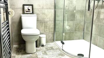 A bathroom with a toilet, a framed picture on the wall, a glass shower enclosure, and patterned floor tiles.
