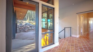 A modern interior with a glass door leading to a stone patio, a staircase, and a hallway with patterned flooring.