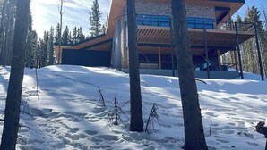 A modern building with a flat roof and large windows, surrounded by snow-covered ground and trees.