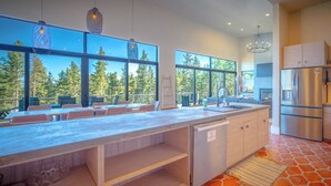 A modern kitchen with a large island, stainless steel appliances, and large windows offering a view of trees.