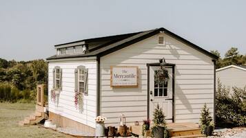 A small, single-story building with a sign reading 'The Mercantile,' featuring a front door, windows, and a small porch area.