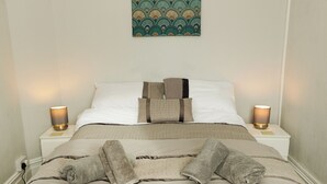 A neatly made bed with a beige and brown patterned bedspread, two pillows, and two bedside lamps on white nightstands. - Seaside Solace: 2BR with Scenic Coastline Views (Llandudno)