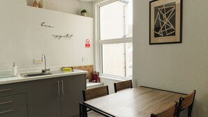 A modern kitchen with a wooden dining table, grey cabinets, a window, and a framed artwork on the wall. - Seaside Solace: 2BR with Scenic Coastline Views (Llandudno)