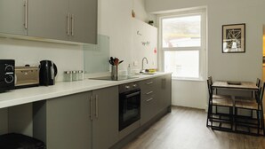 A modern kitchen with grey cabinets, a built-in oven, and a window providing natural light. - Seaside Solace: 2BR with Scenic Coastline Views (Llandudno)