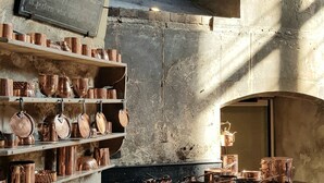A rustic kitchen with copper cookware, a wooden table, and a chalkboard with a message. - Kingfisher Suite - Two-bed Private Apartment (Stamford)