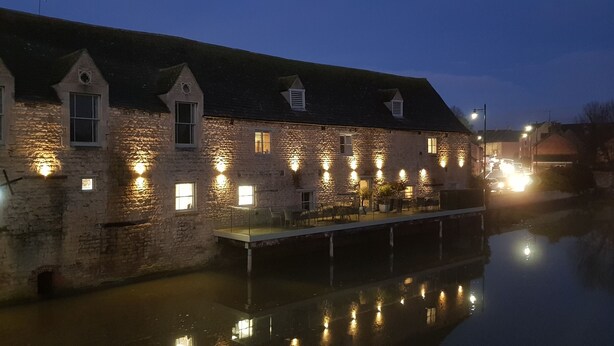 A stone building with multiple windows, a dock, and a calm water body reflecting the lights. - Kingfisher Suite - Two-bed Private Apartment (Stamford)