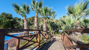 A wooden bridge over a pool area with palm trees and a clear blue sky. - Premium Tent Lodge for Family (Tarragona)
