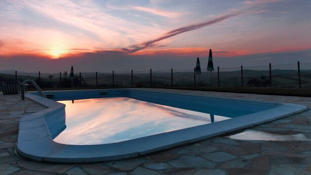 Una piscina con terraza de piedra, rodeada por una valla y con vistas a un paisaje montañoso.