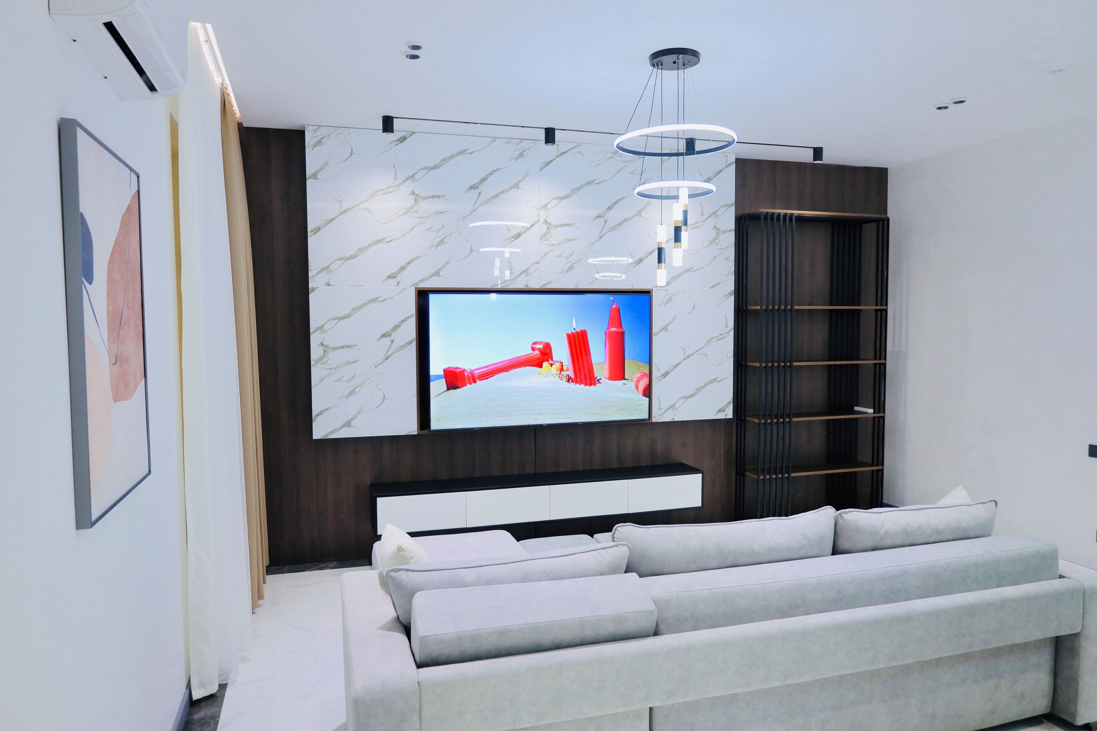 Uma sala de estar moderna com uma grande TV de tela plana presa na parede, que tem um padrão semelhante ao mármore, um sofá cinza e um armário de madeira escura com prateleiras.