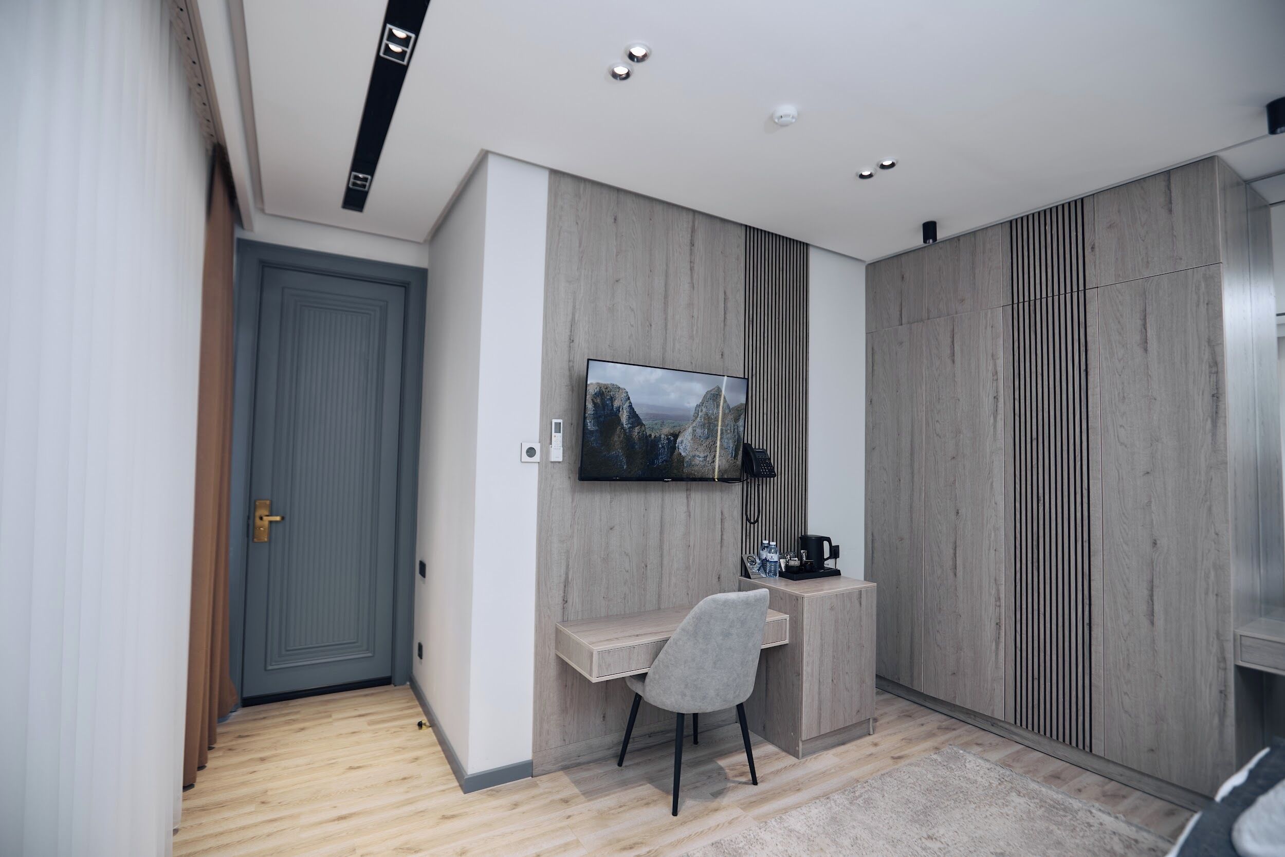 A modern room with a grey door, a mounted TV, a wooden desk, and a grey chair.