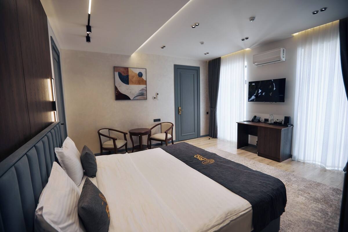 A hotel room with a bed, a desk, a TV, a chair, and a painting on the wall.