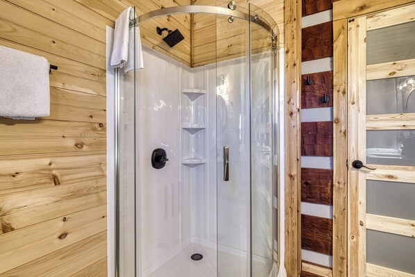 Eine Duschkabine mit Glaswänden und Holzinnenraum, ein weißes Handtuch an der Wand und eine Holztür mit Glasscheiben.