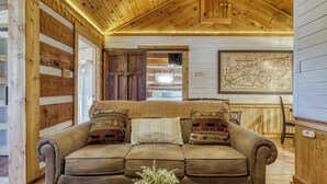 A cozy living room with a wooden ceiling, a brown sofa with patterned cushions, a map on the wall, and a small table with a vase. - A Timber Hideaway, Cozy Cabin Retreat in the Smokies – Comfort & Fun for All! (Sevierville)