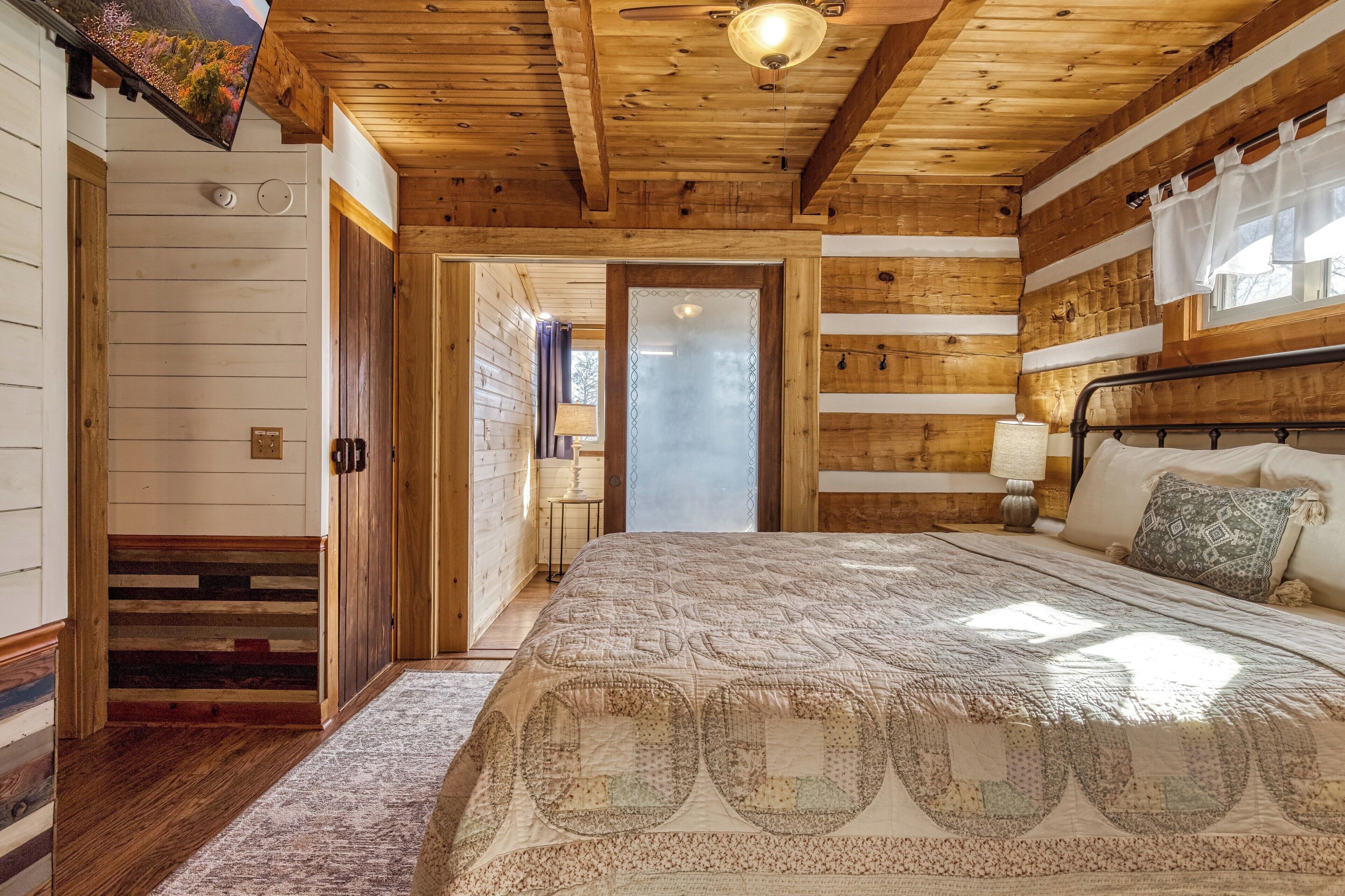 Une chambre à coucher aux murs lambrissés, avec un lit, une table de chevet et une fenêtre avec des rideaux.