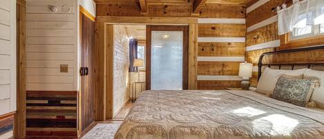 Quarto com painéis de madeira, uma cama, uma mesa de cabeceira e uma janela com cortinas.