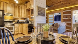 A wooden cabin interior with a dining area, kitchen, and a cozy living space. - A Timber Hideaway, Cozy Cabin Retreat in the Smokies – Comfort & Fun for All! (Sevierville)