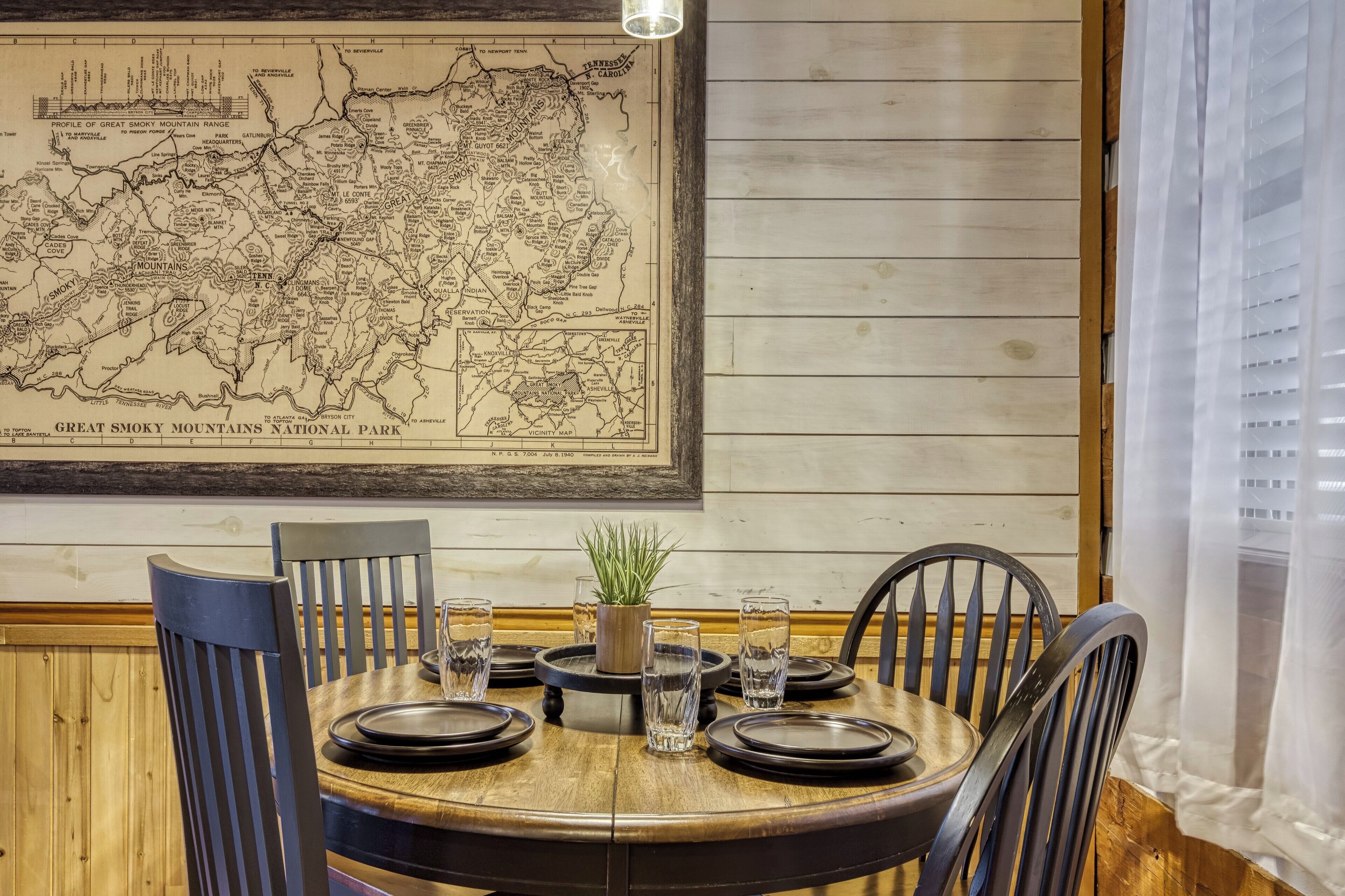 A dining table set with plates, glasses, and a potted plant, with a map of the Great Smoky Mountains National Park on the wall.