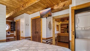 A cozy room with a large bed, wooden ceiling, and a mounted TV displaying a scenic view. - A Timber Hideaway, Cozy Cabin Retreat in the Smokies – Comfort & Fun for All! (Sevierville)