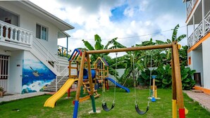 A playground with swings and slides, surrounded by a house with a balcony and a mural on the wall. - HOTEL EL PIRATA MORGAN (Providencia)