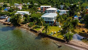 An aerial view of a coastal property with multiple buildings, a clear beach, and lush greenery. - HOTEL EL PIRATA MORGAN (Providencia)