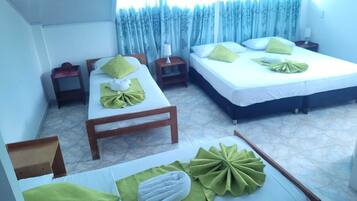A hotel room with two beds, each with green towels and pillows, a small wooden table, and a nightstand with a lamp.
