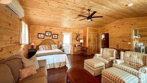 Accogliente interno di una baita in legno con un letto, un divano, un'area da pranzo e una ventola a soffitto.