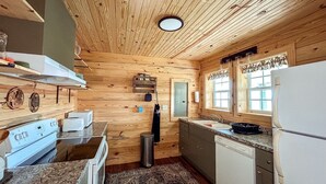 Cucina di una baita in legno con forno, lavello e frigorifero.