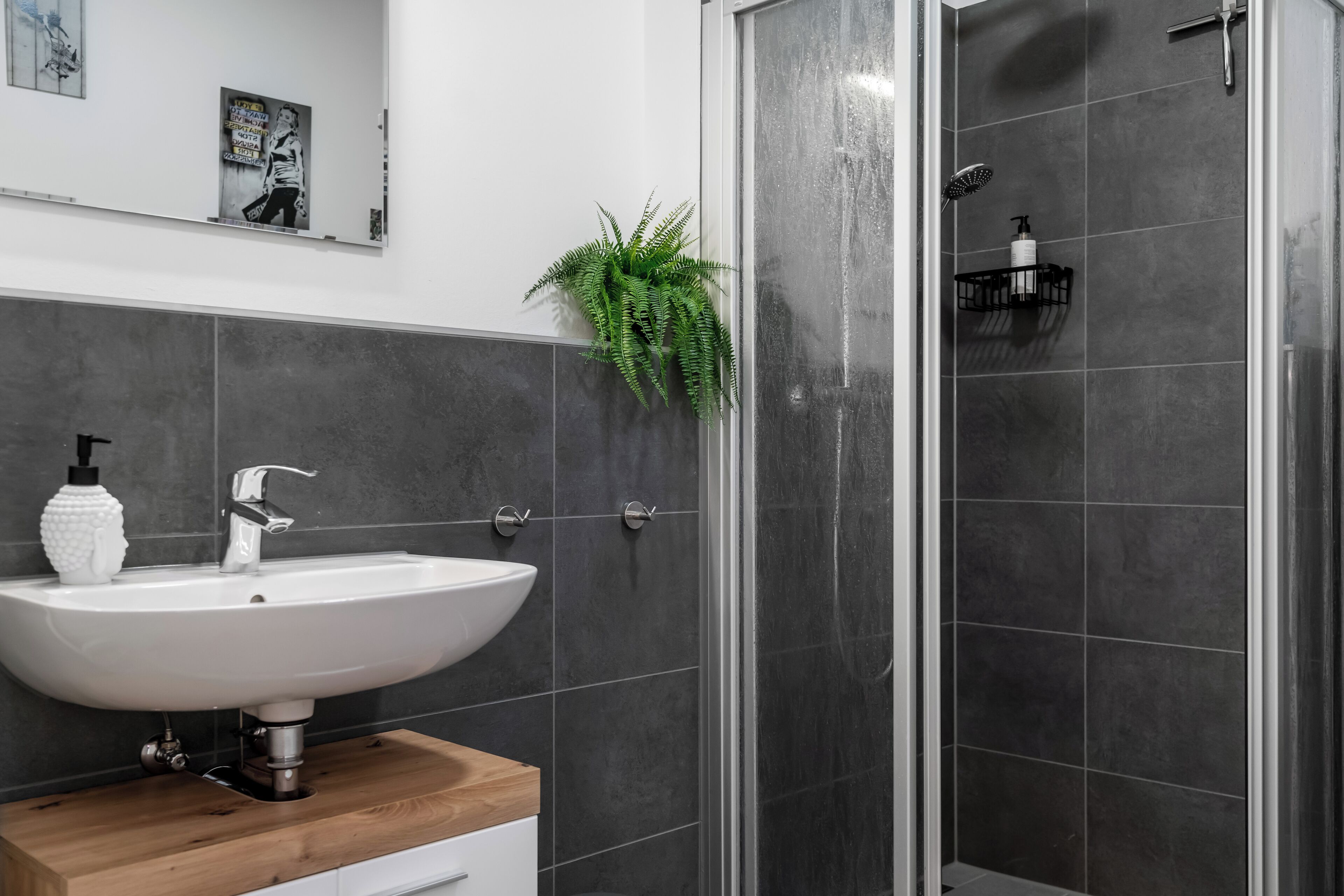 A modern bathroom with a white sink, wooden countertop, and a shower with a glass door.