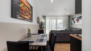A modern living room with a grey sofa, a dining table with chairs, and a large abstract painting on the wall. - Design luxury, fully equipped, 30min Leipzig Hbf 8 (Schkeuditz)