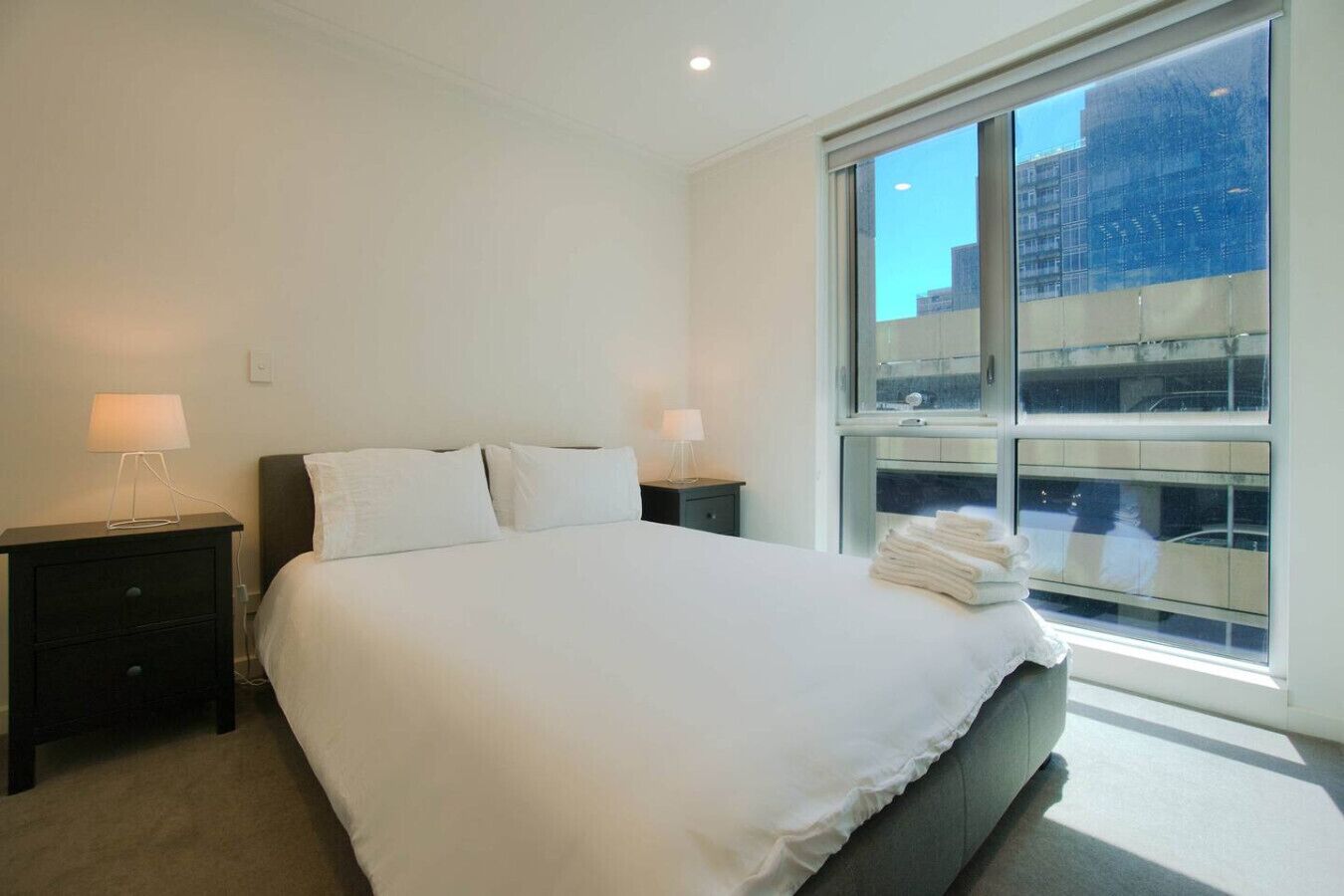 Une chambre d’hôtel moderne avec un grand lit, deux tables de chevet et une fenêtre donnant sur la ville.