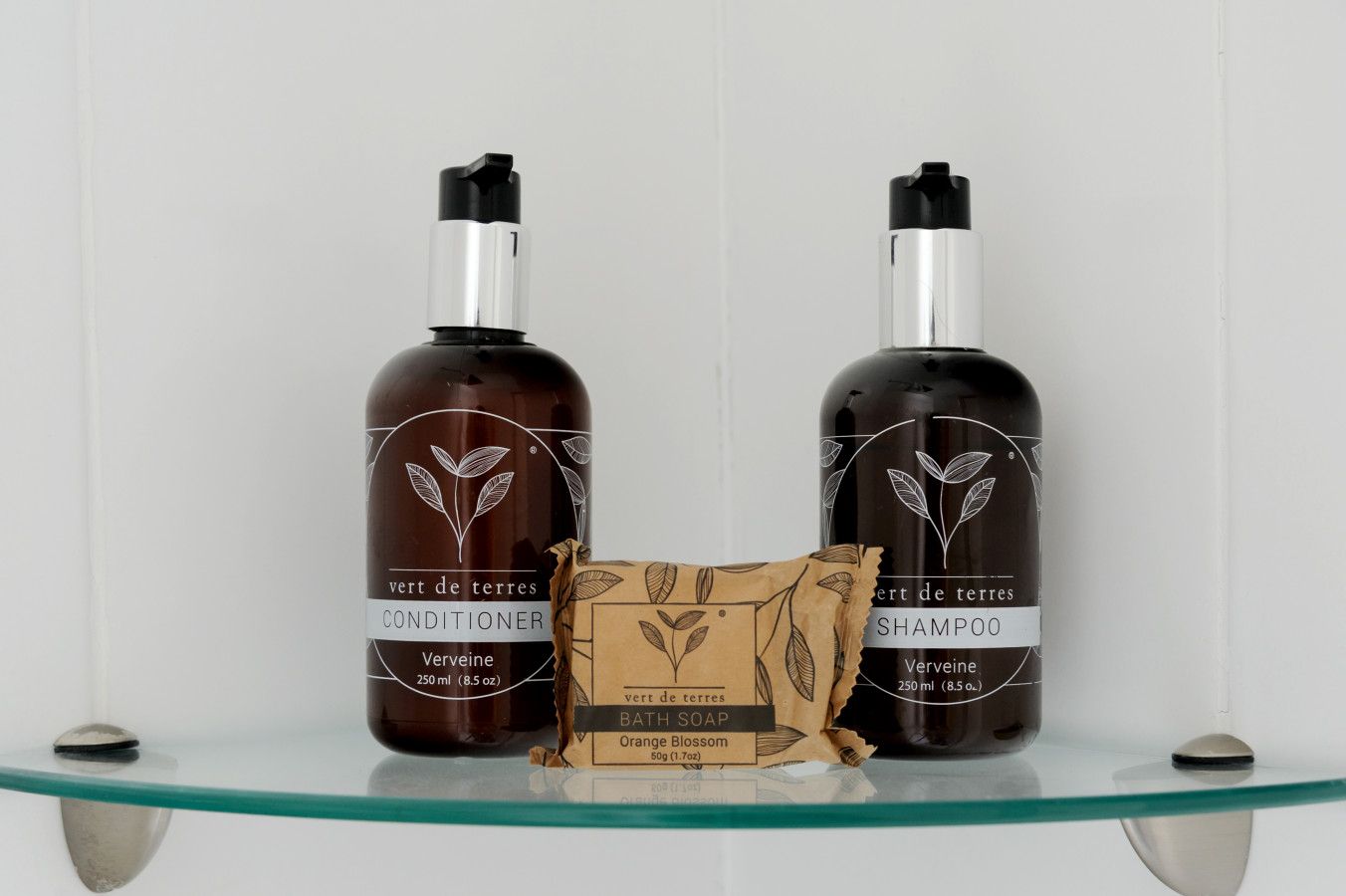 Duas garrafas de condicionador e shampoo, uma pequena caixa de sabonete de banho e uma prateleira de vidro.