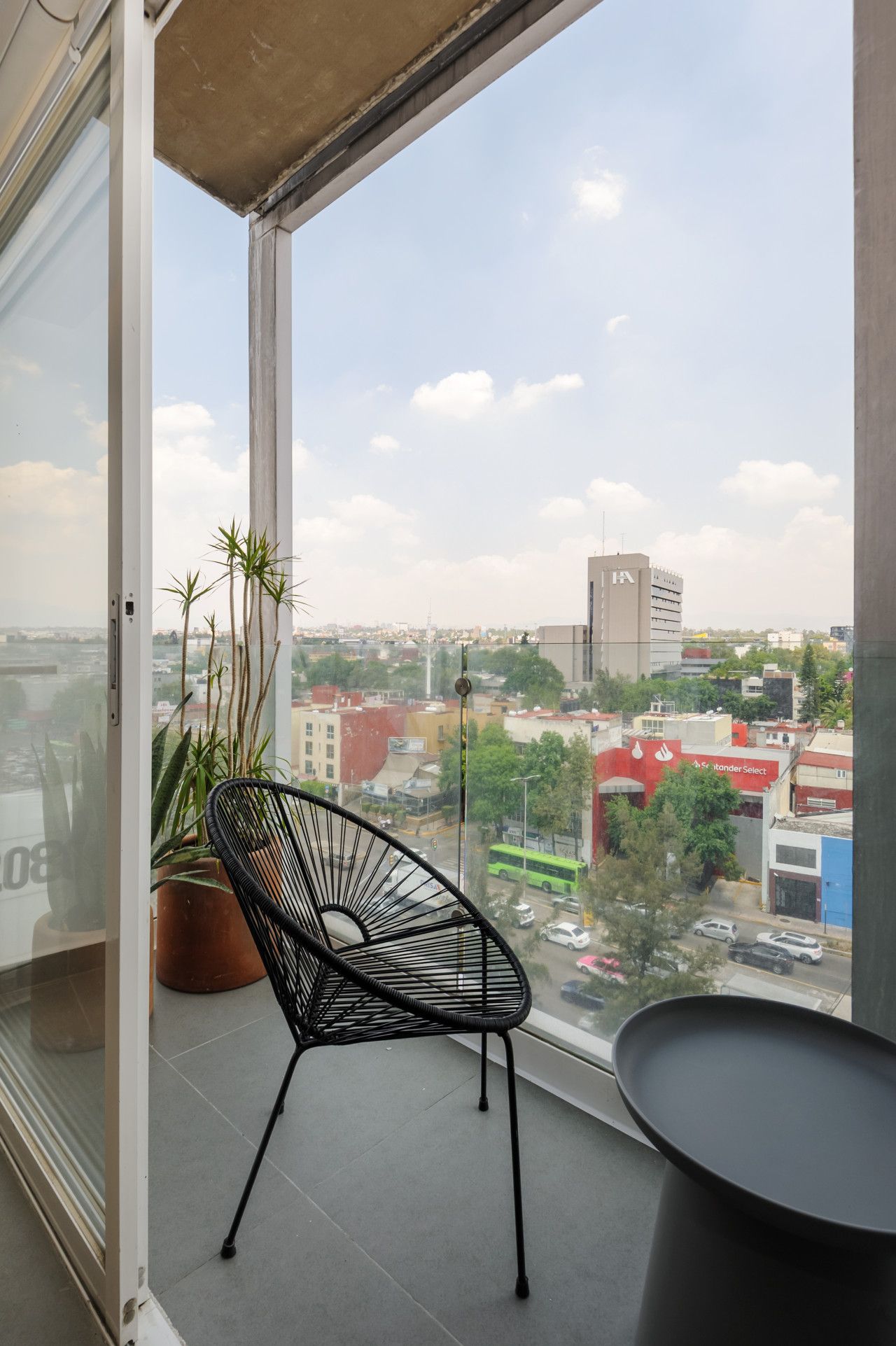 Un balcon avec une chaise noire, un pot de fleurs et une vue sur le paysage urbain.