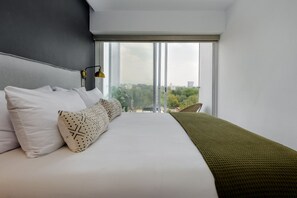 Ein modernes Hotelzimmer mit einem großen Bett, Blick auf die Stadt und einem Balkon mit einem Stuhl.