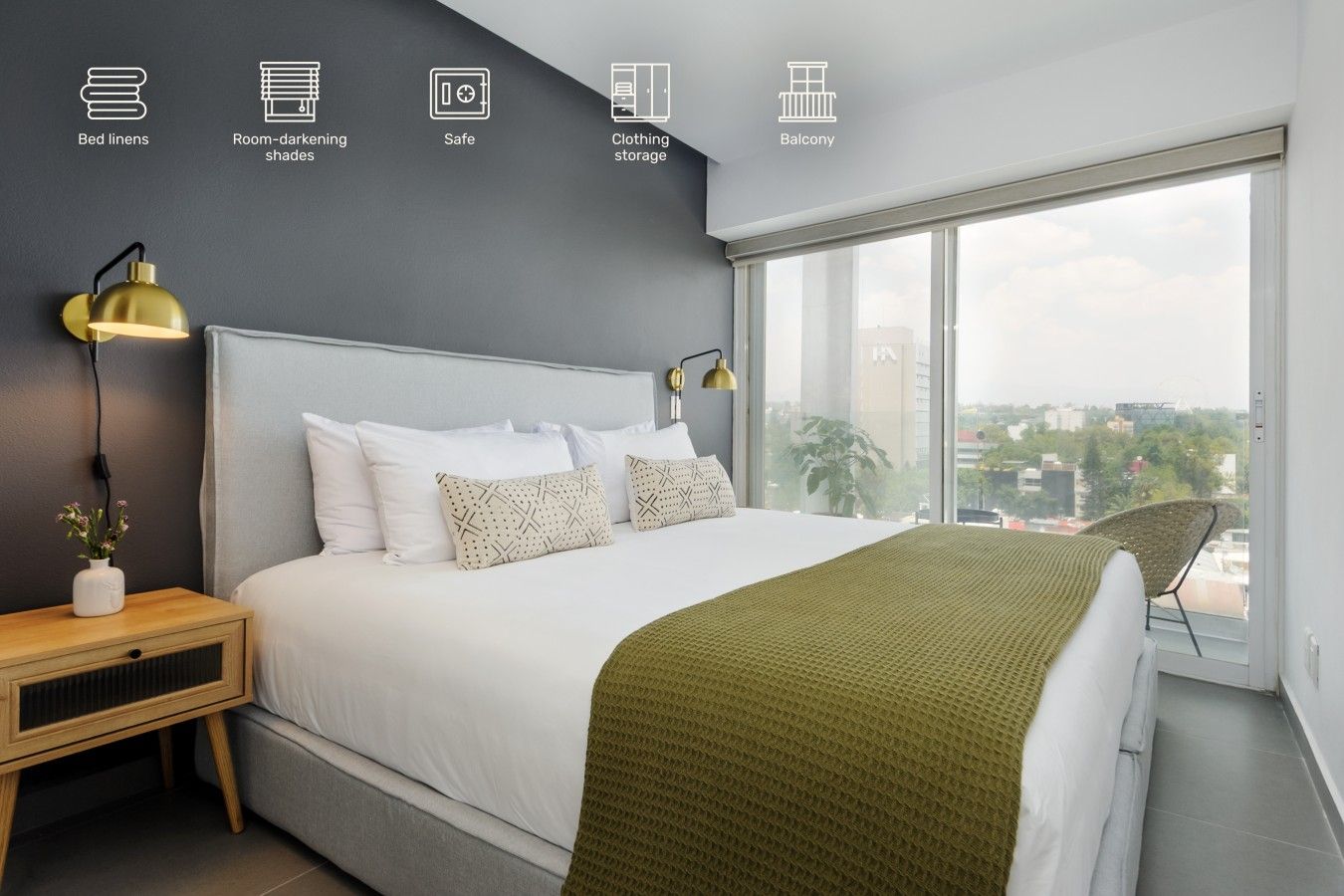 A modern bedroom with a large bed, bedside lamps, a view of the city through a large window, and a balcony.