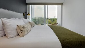 A modern hotel room with a large bed, a view of the city, and a balcony with a chair. - Modern 2BR Duplex, with balcony. (Ciudad de México)