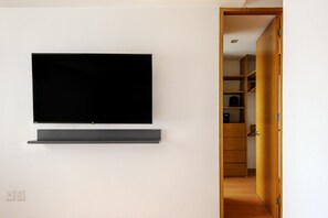 Ein modernes Zimmer mit einem flachbildfernseher an der Wand, einer Holztür zu einem Schrank und einer weißen Wand.