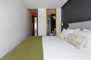 A hotel room with a bed, a green throw blanket, white pillows, and a black lamp.