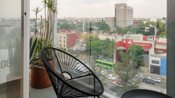 A balcony with a black chair, a potted plant, and a view of a cityscape. - Modern 2BR Duplex, with balcony. (Ciudad de México)