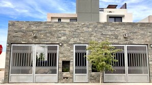 A modern building with stone facade, large windows with metal bars, and a chimney. - Casa de las Olas (La Paz)