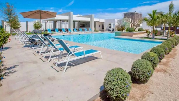 A pool area with lounge chairs and umbrellas, surrounded by neatly trimmed bushes and a clear blue sky. - Casa de las Olas (La Paz)